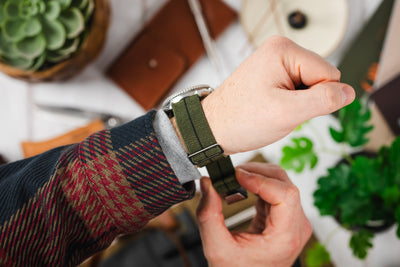 A mans wrist wearing an elasticated MN strap in green.