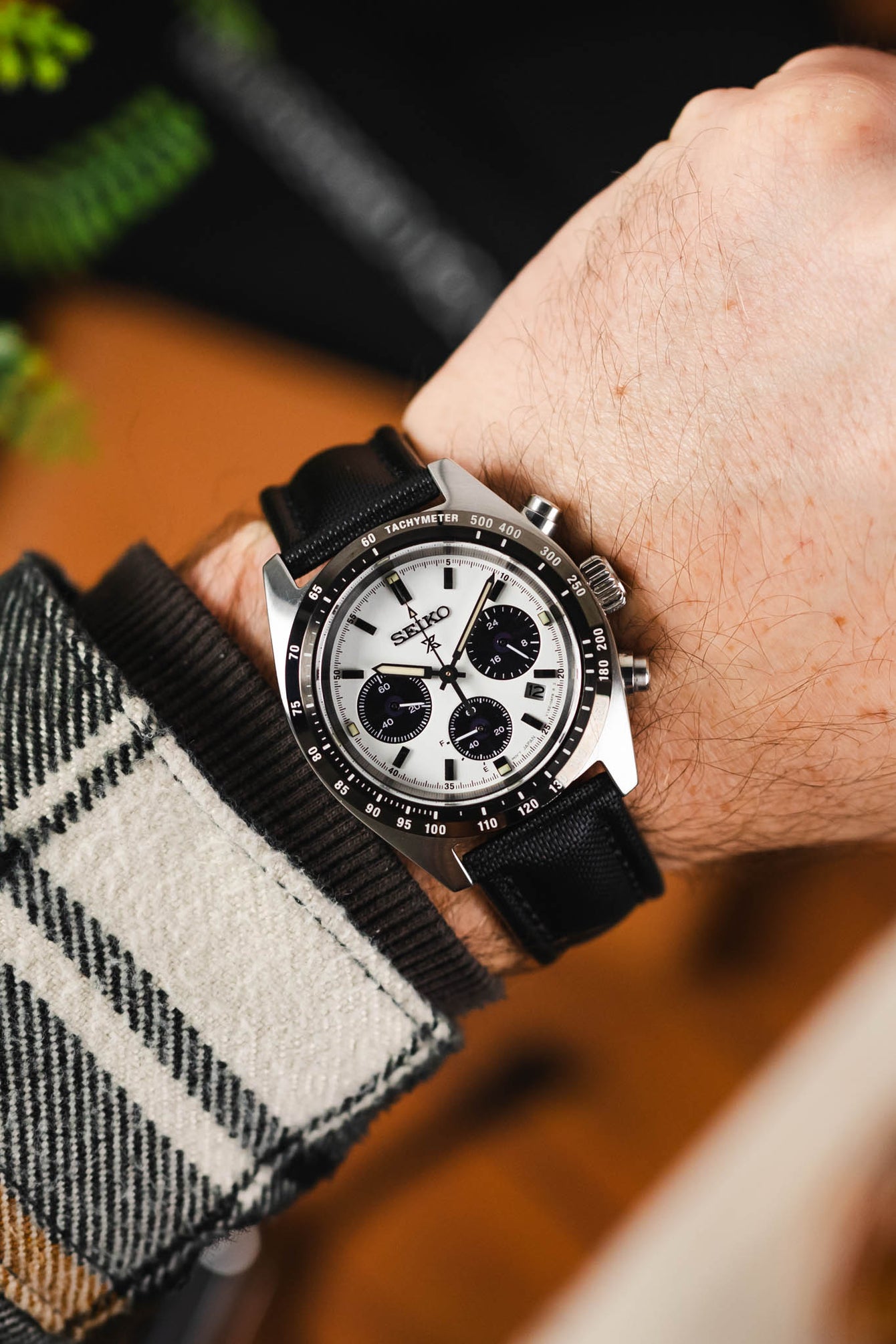 Black Artem sailcloth watch strap with black stitching fitted to a Seiko Prospex with panda dial and silver pusher and crown, on wrist with check flannel shirt.