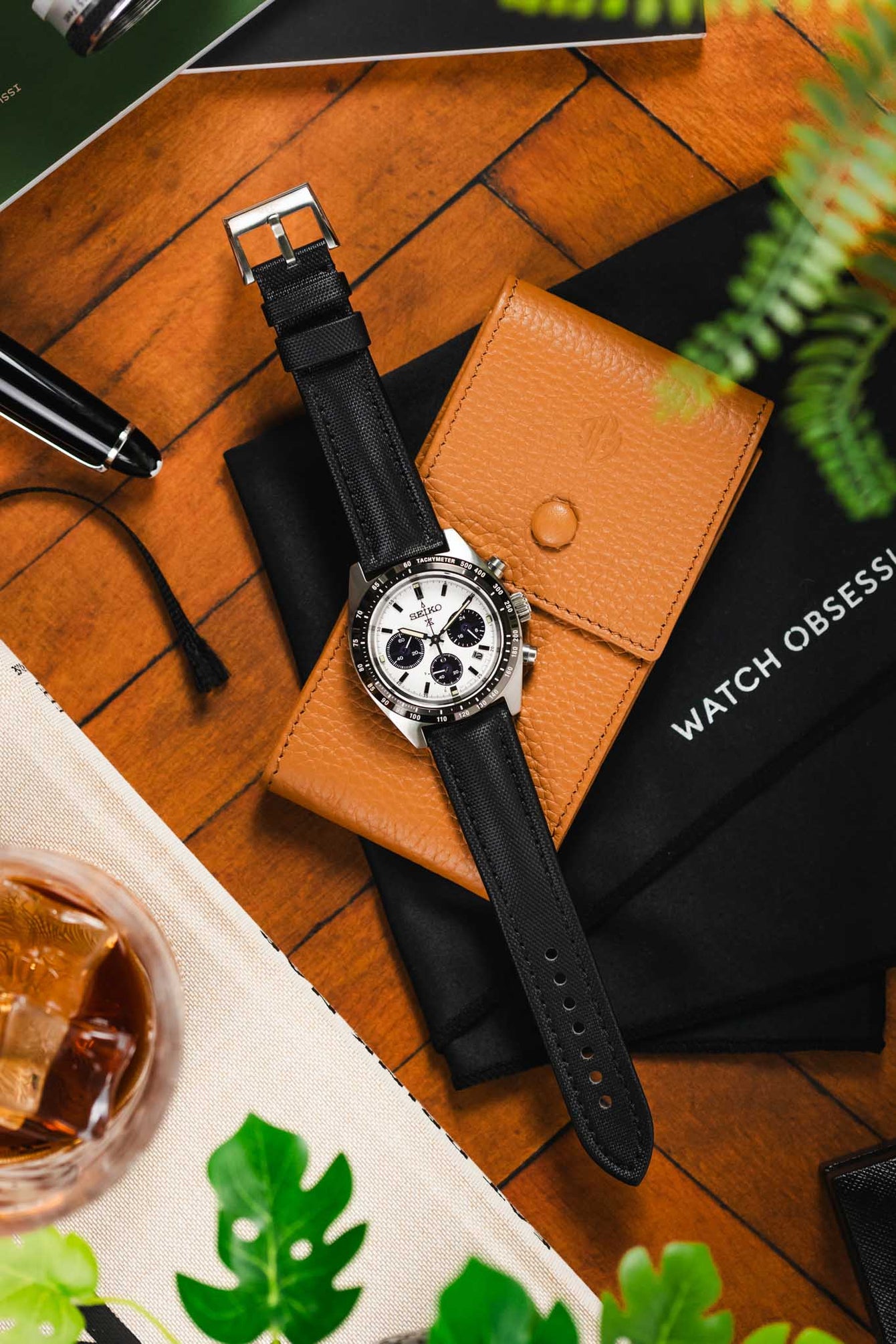 High angle shot of face up panda Seiko Prospex speedetime and black chronograph with Artem Straps classic sailcloth on wooden brown table and beige leather watch case.