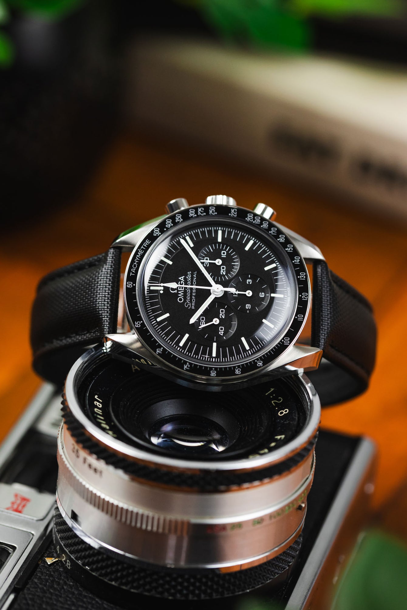 Curved Artem Loop-Less Black Sailcloth strap fitted to Omega Speedy in black on top of Camera. 