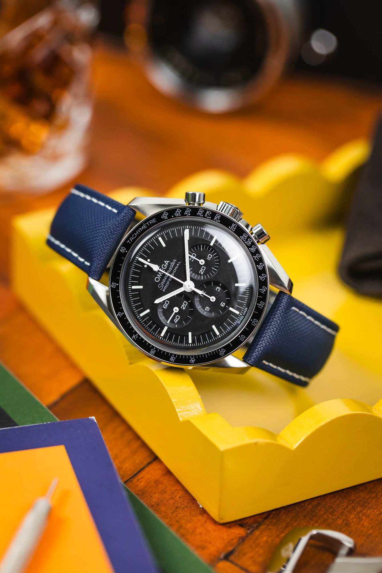 Curved Artem Navy Blue Loop-less sailcloth strap with white stitching fitted to Black Omega Speedmaster Moonwatch on yellow box