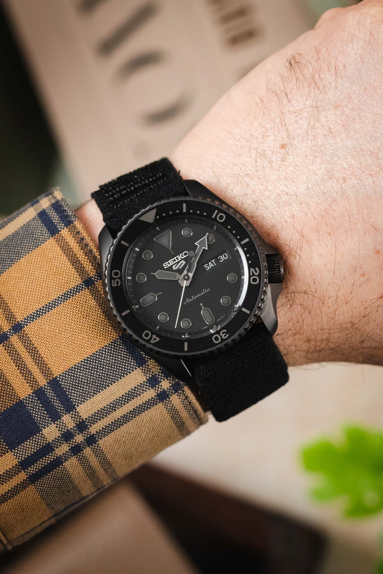 A Seiko 5 Sports SRPD79K1 watch with a black case and dial, worn on a wrist with a black fabric strap, showcasing the watch's design and fit.